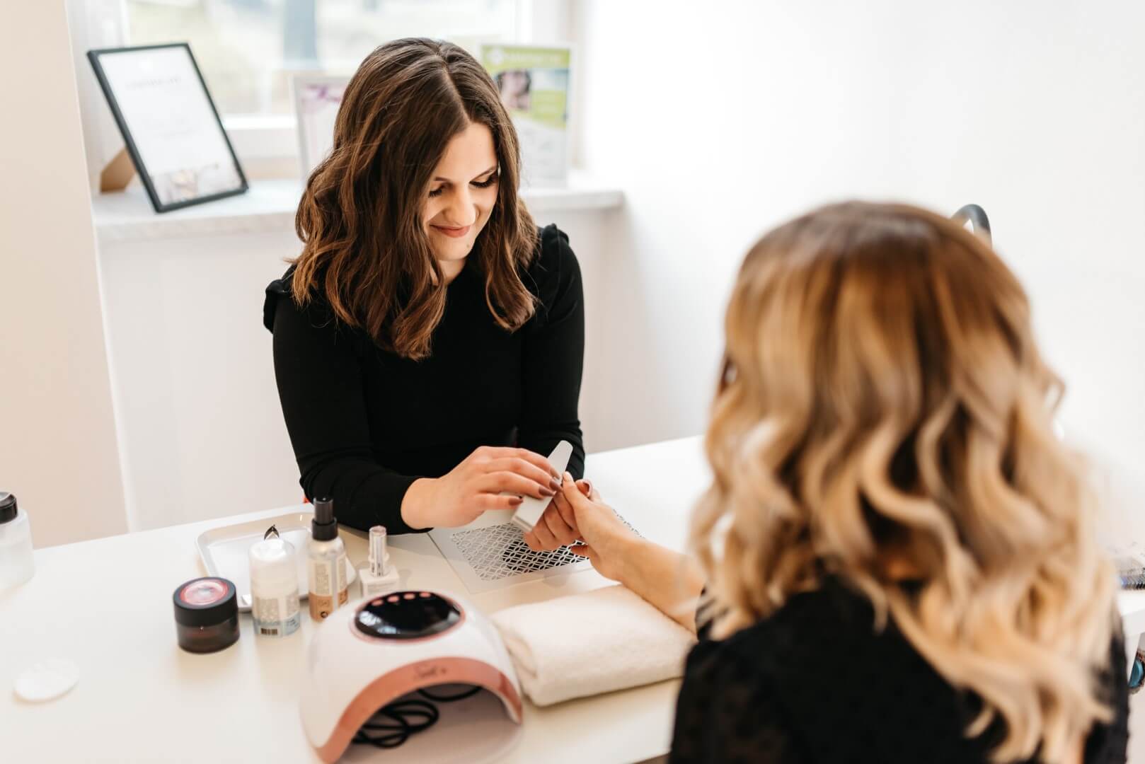 Nohtna stilistka in stranka med urejanjem nohtov.